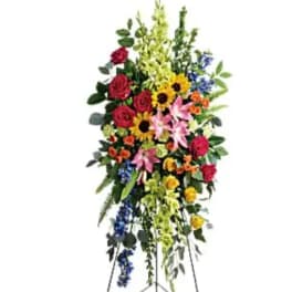 Tall standing floral spray with red roses, lilies, sunflowers, and blue accents