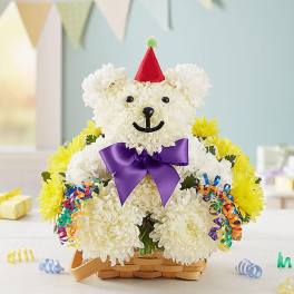 White flower teddy bear in a basket with a purple bow and party hat