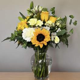 Bouquet of yellow roses, sunflowers, and white carnations in a glass vase