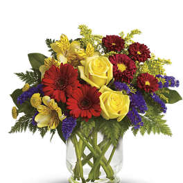 Mixed bouquet of yellow roses, red daisies, and purple filler in a glass vase