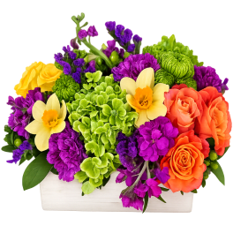 Low rectangular arrangement with orange roses, yellow daffodils, green hydrangeas, and purple flowers.