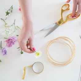 Hands arranging small flowers with scissors and floral wire on a white table