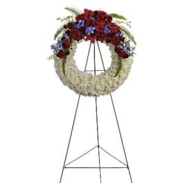 Standing funeral wreath with red and white flowers and blue accents on an easel