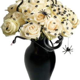 Cream roses in a black vase with decorative spiders and snakes