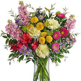 Mixed bouquet of pink, yellow, purple, and white flowers in a clear glass vase
