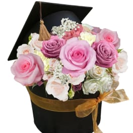 Pink and lavender roses in a black graduation cap box with a gold ribbon