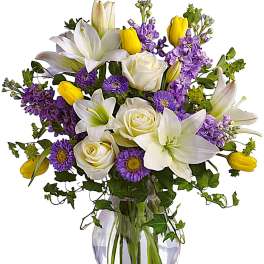 Bouquet of white lilies, roses, purple flowers, and yellow tulips in a glass vase