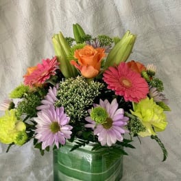 Mixed bouquet in a green glass vase with pink, orange, and lavender flowers