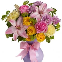 Pink and yellow mixed bouquet in a lavender vase with a pink ribbon