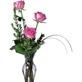 Pink roses arranged in a clear glass vase with greenery