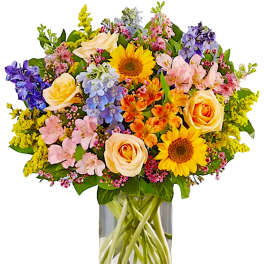 Colorful mixed bouquet with roses, sunflowers, and delphinium in a glass vase