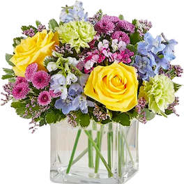 Mixed bouquet of yellow roses, blue flowers, and pink blooms in a clear glass vase