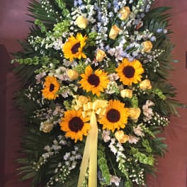 Standing floral spray with sunflowers, yellow roses, and a yellow ribbon