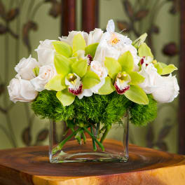 White roses and green orchids in a clear glass vase