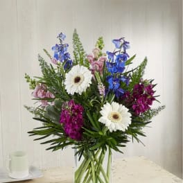 Mixed bouquet with white daisies, blue and pink flowers in a clear glass vase