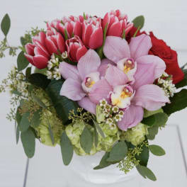 Bouquet of pink tulips, orchids, and red roses in a white vase