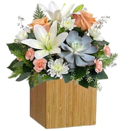 Flower arrangement with white lilies, peach roses, and a succulent in a wooden cube vase