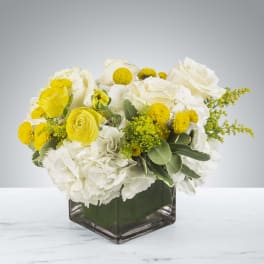 Low arrangement of white hydrangeas and roses with yellow blooms in a square glass vase