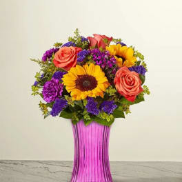 Bouquet of sunflowers, roses, and purple flowers in a pink vase