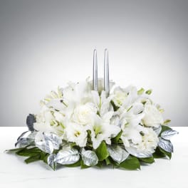 Low white lily and rose centerpiece with silver leaves and two tall silver taper candles