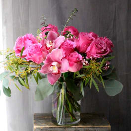Pink roses and orchids arranged in a clear glass vase