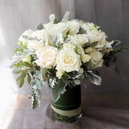 White roses arranged in a glass vase with silvery foliage