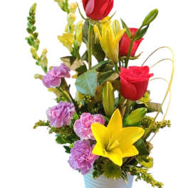 Tall mixed arrangement of red roses, yellow lilies, and purple carnations in a white pot