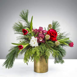 Asymmetrical holiday arrangement with red roses, tulips, orchids and a white bloom in a gold vase