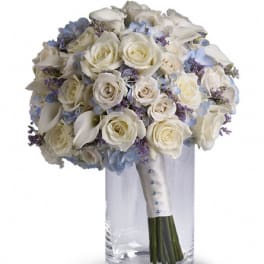 White rose bouquet with pale blue flowers in a clear glass vase