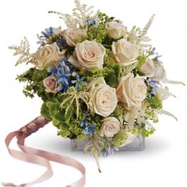 Hand-tied bouquet of cream roses with blue flowers and a pink ribbon