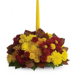 Yellow candle in a low arrangement of red and yellow flowers