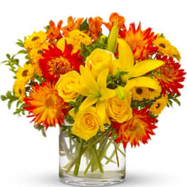 Yellow roses and lilies in a clear glass vase with red and orange flowers