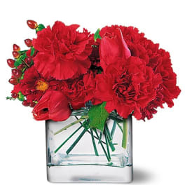 Red carnations and tulips arranged in a clear glass vase
