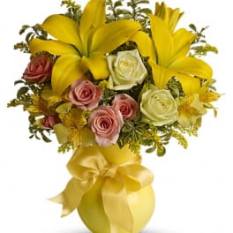 Yellow lilies and pink roses arranged in a gold vase with a ribbon bow.