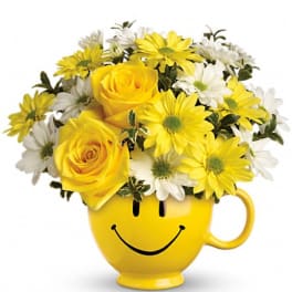 Yellow and white flowers arranged in a smiley-face mug