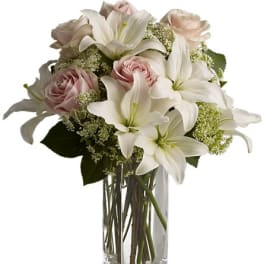 White lilies and pale pink roses in a clear glass vase