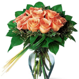 Peach roses arranged in a clear glass vase with greenery