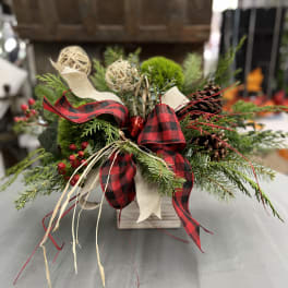 Holiday arrangement of evergreen branches with red plaid ribbon in a wooden container
