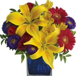 Colorful bouquet of lilies, roses, and daisies in a blue glass vase