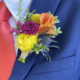 Colorful boutonniere with yellow, orange, purple and blue blooms on a navy suit jacket.