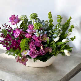 Low white ceramic arrangement with purple roses, orchids, and white tulips in an asymmetrical design