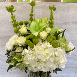 Tall white and green flower arrangement with hydrangeas and roses in a clear glass vase
