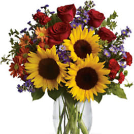 Bouquet of sunflowers, red roses, and purple flowers in a glass vase