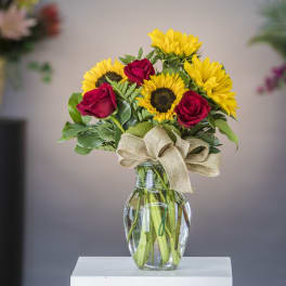 Sunflowers and red roses in a clear glass vase with a burlap bow