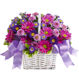 Pink and purple flowers in a white wicker basket with lavender ribbons