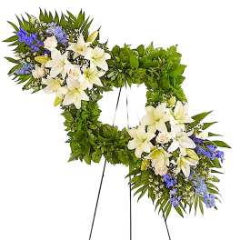 Heart-shaped floral wreath with white lilies and blue flowers on a stand