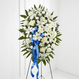 White floral standing spray with a blue ribbon on a black easel