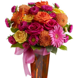 Mixed bouquet of roses and daisies in an amber vase with a pink ribbon