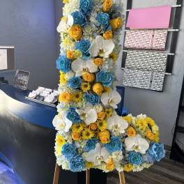 Tall floral standing arrangement with blue, yellow, and white blooms on an easel
