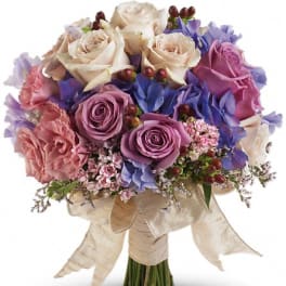Bouquet of cream, pink, and purple roses with blue flowers and a ribbon wrap